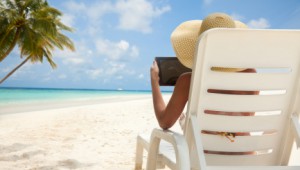 Woman with tablet computer on the beach sitting in the deck chair